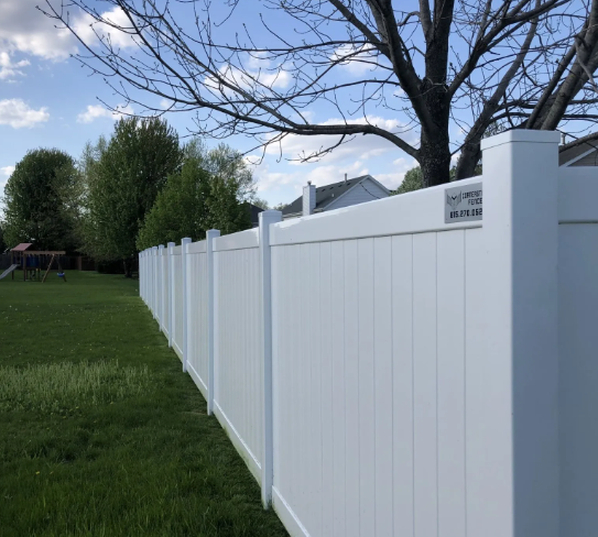 White vinyl fence bordering a grassy backyard under a partly cloudy sky.