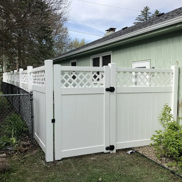 White vinyl fence with lattice top sections and gate attached to a green house.