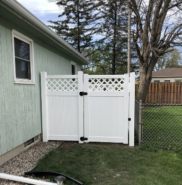 White vinyl gate attached to a light green house with diamond lattice details.
