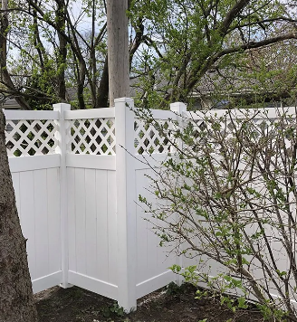 White vinyl fence with lattice top section, next to a tree and some bushes.