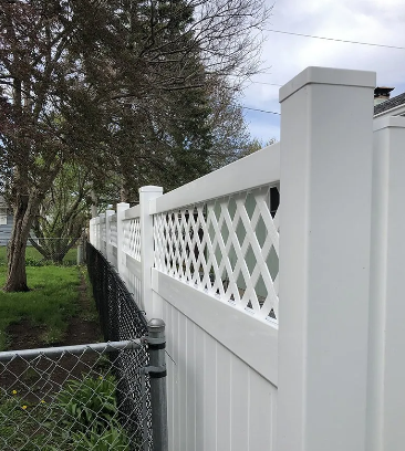 White lattice-topped privacy fence with vertical panels, built above a chain-link fence, in a yard.