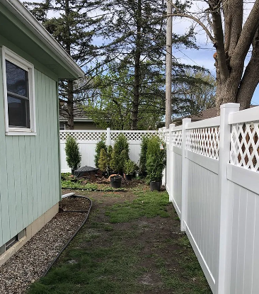 Side yard with green house, white fence, trees, and dirt path.