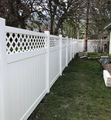 White vinyl privacy fence with lattice top running along a green lawn and trees.