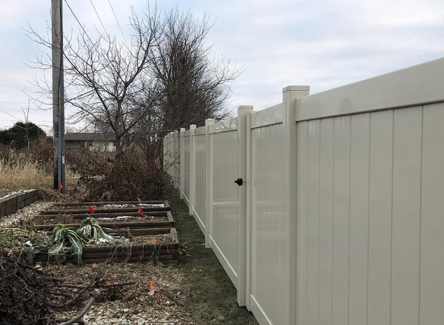 Cream-colored vinyl fence bordering a garden, under a cloudy sky.