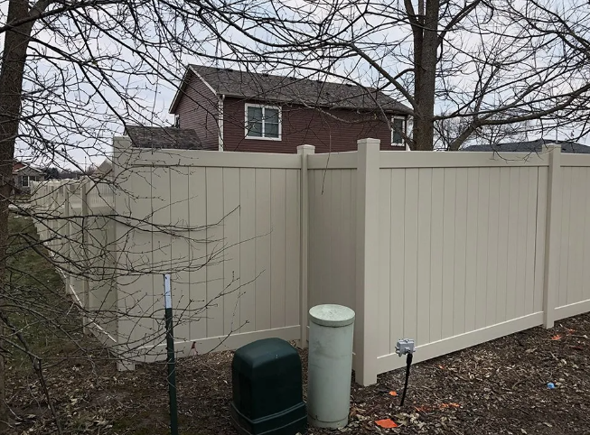 Beige vinyl fence in a yard, with a house visible in the background.