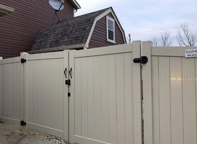 Cream-colored vinyl fence with two gates, black hardware, and an adjacent brown house with a satellite dish.
