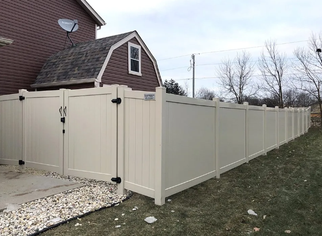 Beige vinyl privacy fence surrounding a grassy yard and part of a brick house with a satellite dish.
