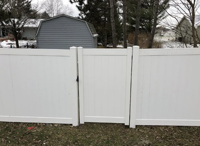 White vinyl fence with a gate in a backyard, grey shed in the background.