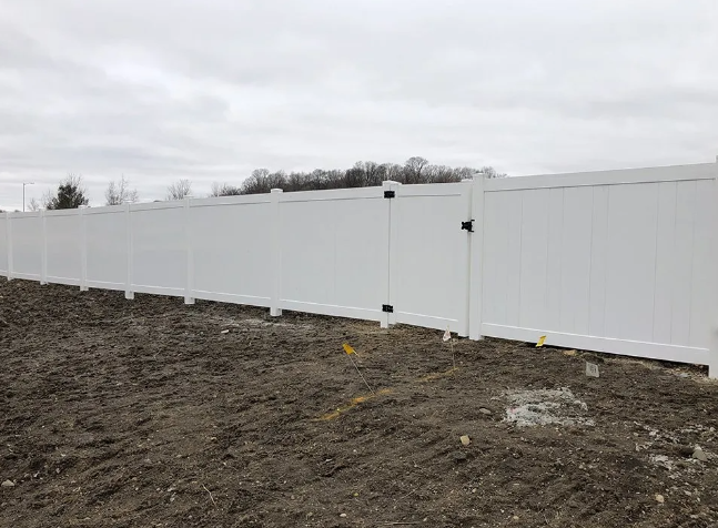White vinyl fence with gate in a field under overcast sky.