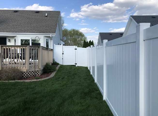 White vinyl fence in backyard, connecting two houses; green lawn and partly cloudy sky.