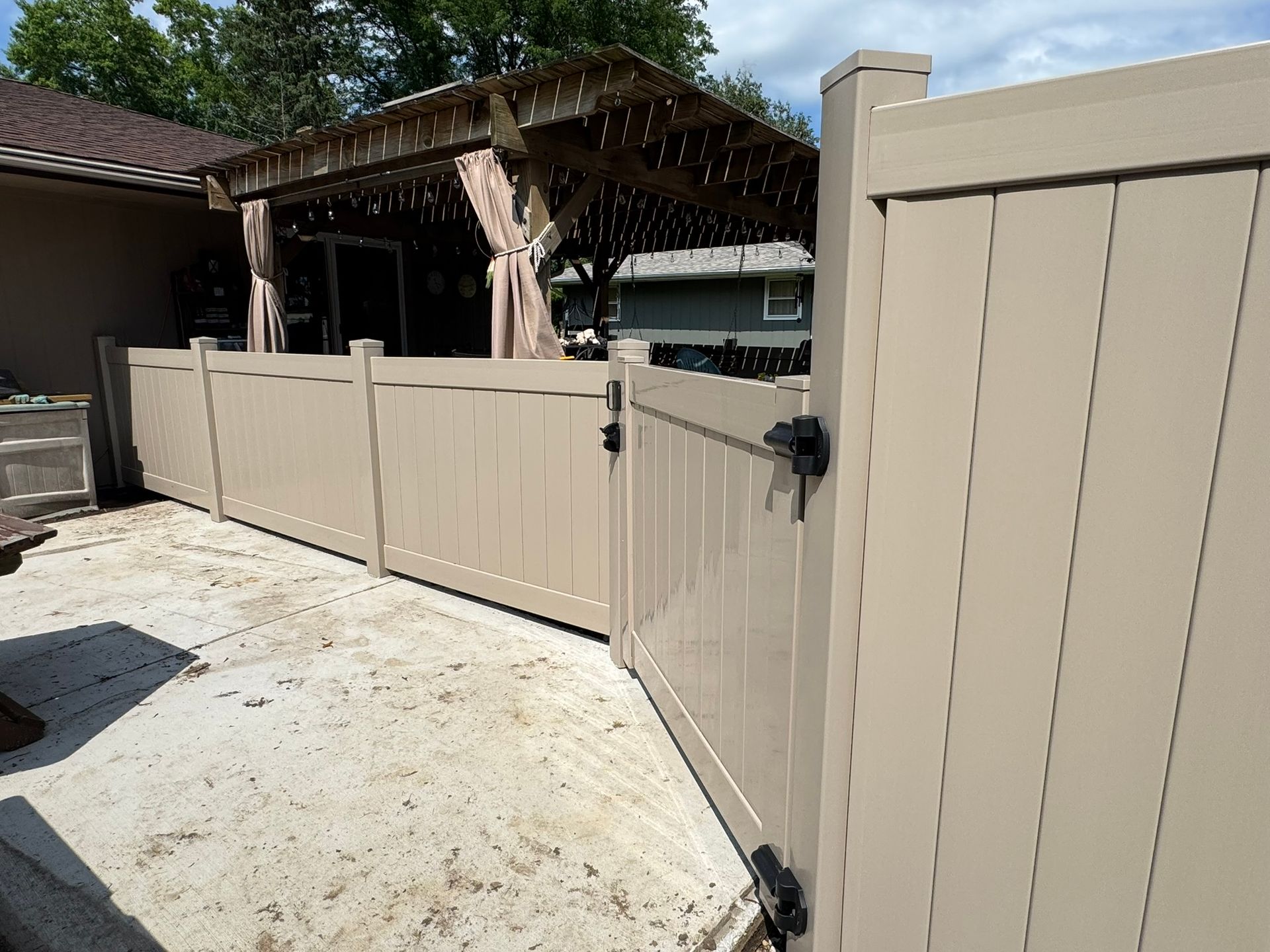 Beige vinyl fence with a gate, next to a patio with a pergola.