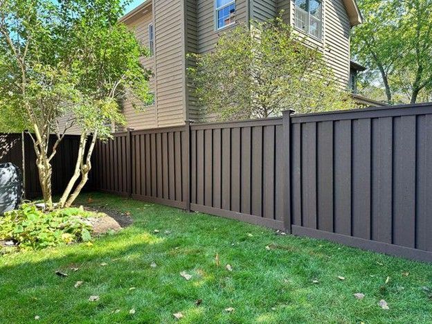 Brown privacy fence in a grassy backyard, adjacent to a two-story house with green foliage.