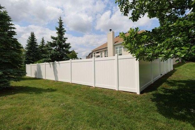 White vinyl fence surrounds a green lawn, with trees and a house in the background under a cloudy sky.