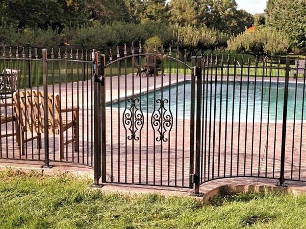 Black metal fence and gate surrounding a swimming pool. Decorative scrollwork on gate.