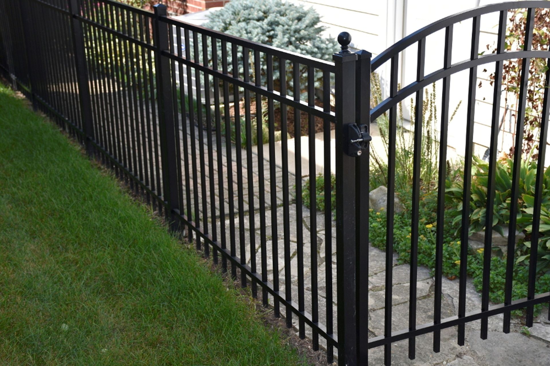 Black metal fence along a grassy lawn, with a gate leading to stone steps.