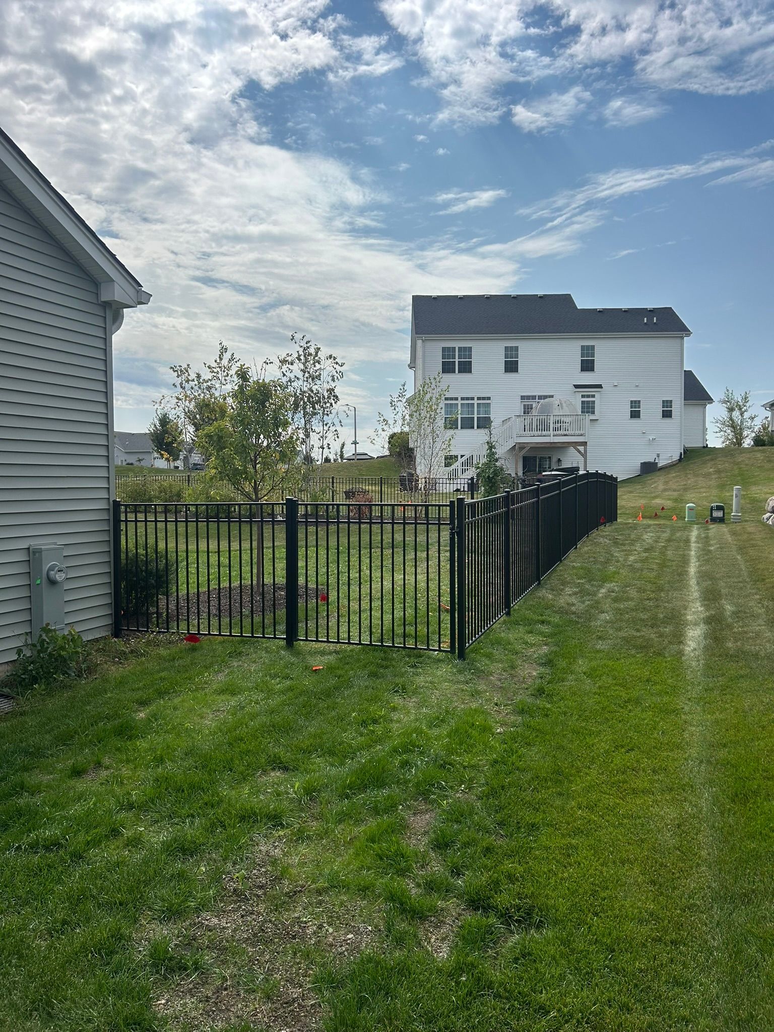 Black metal fence bordering a backyard with a house on a sunny day.