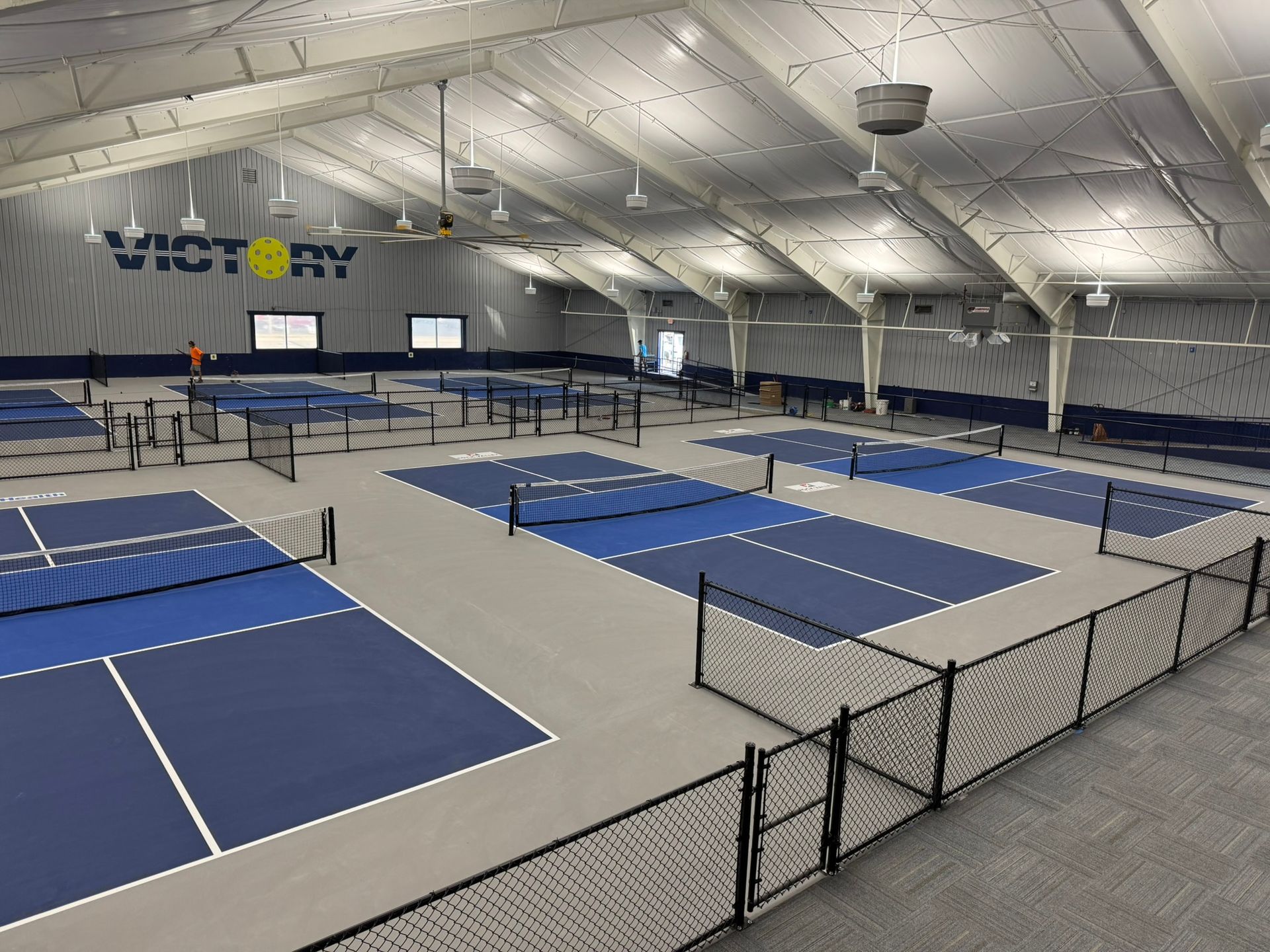 Indoor pickleball court with multiple courts, navy blue and gray color scheme, 