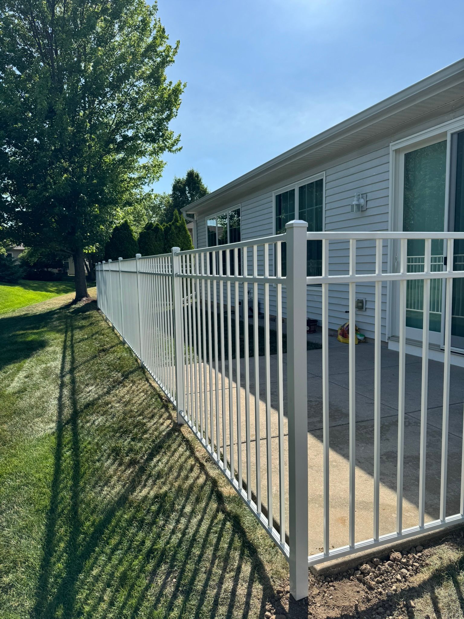 White picket fence alongside a light-colored building with a sunny blue sky.