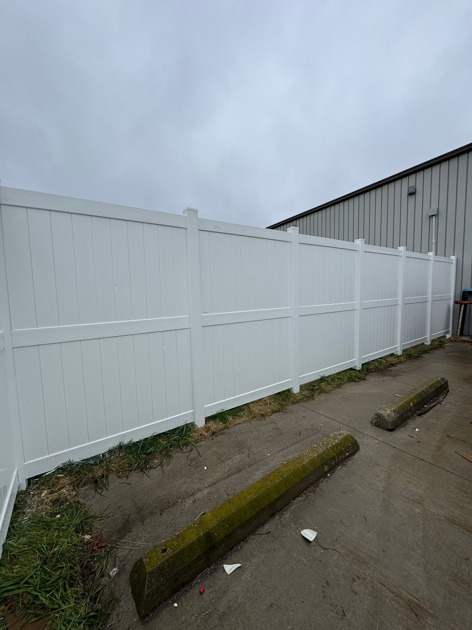 White vinyl fence along a parking area, against a building. Overcast sky.