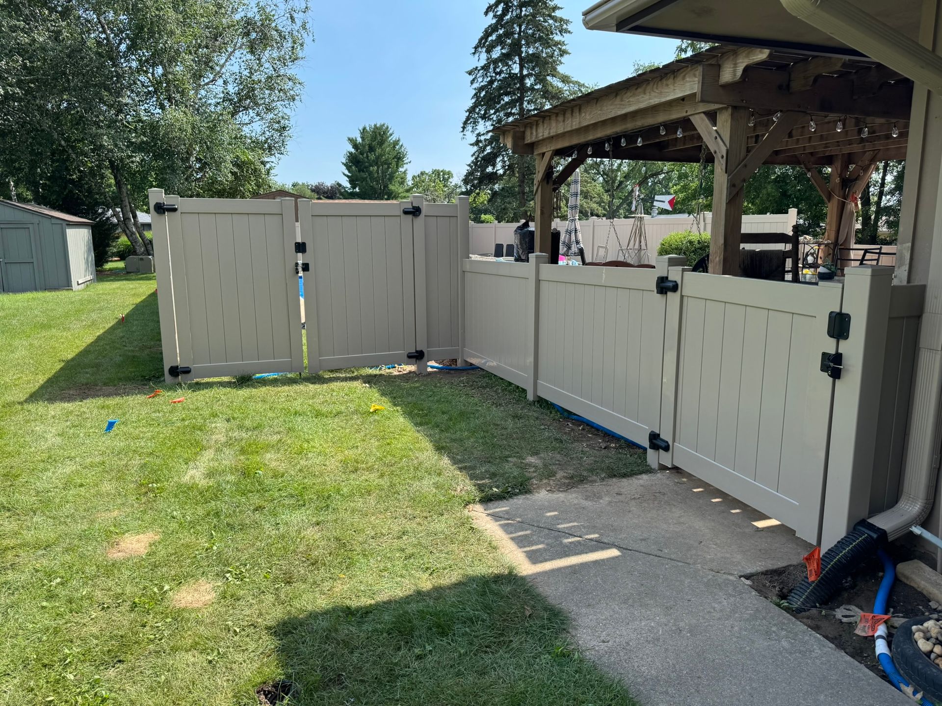 Beige vinyl fence enclosing a backyard with a gazebo, grass, and concrete patio.