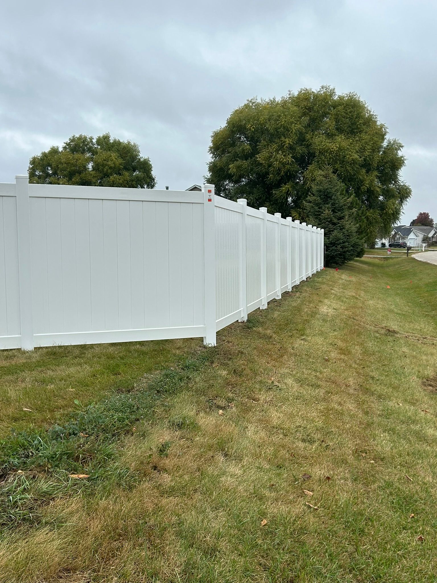 White fence along grassy yard with tree and cloudy sky.
