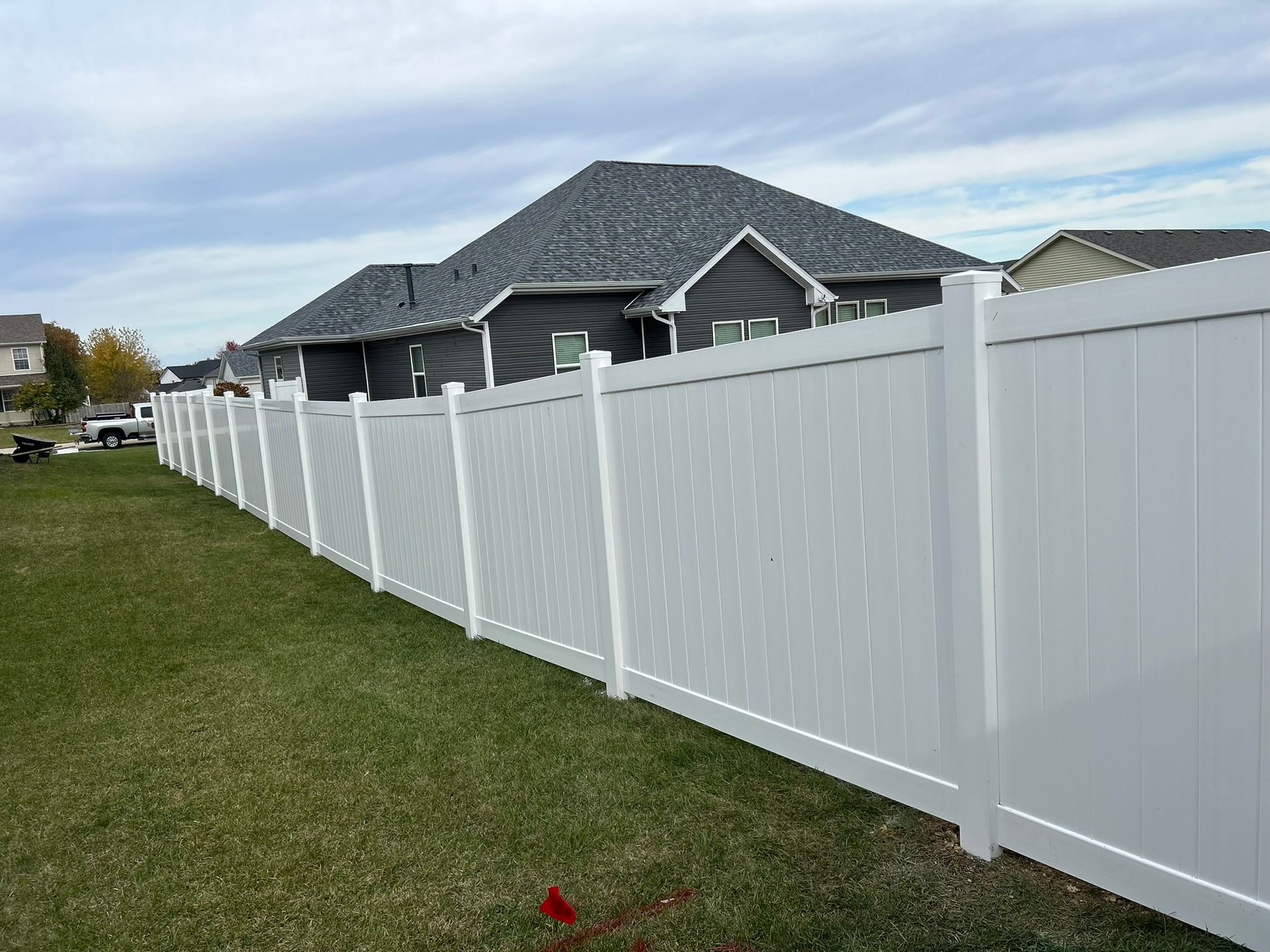 White vinyl fence enclosing a green lawn; a gray house is in the background.