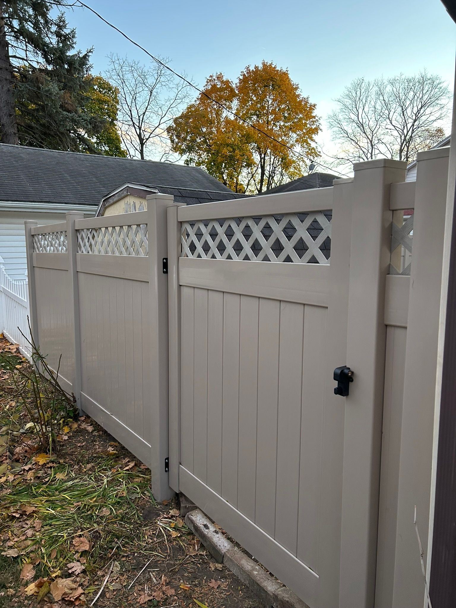Beige vinyl fence with latticework top and closed gate, outdoors on a sunny day.