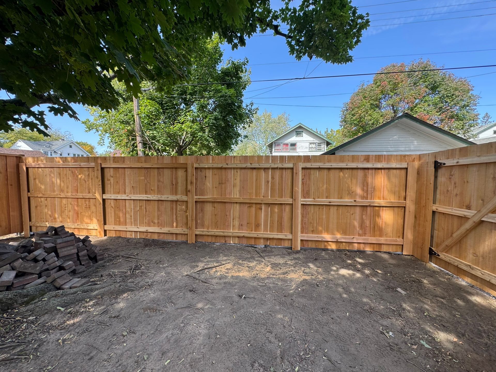 Wooden fence enclosing a dirt backyard; blue sky and trees in the background.