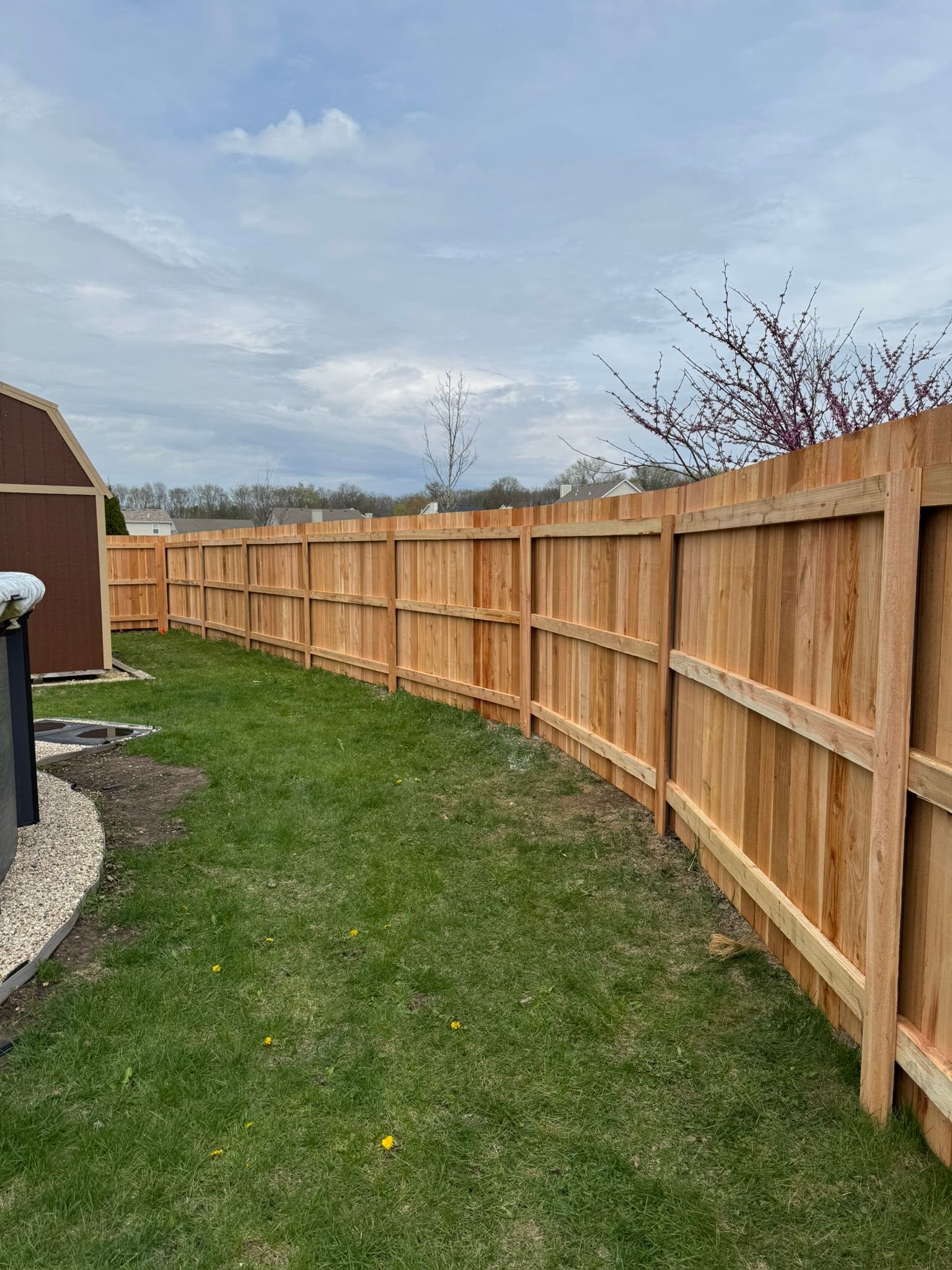 Wooden fence curves around a grassy backyard under a cloudy sky.
