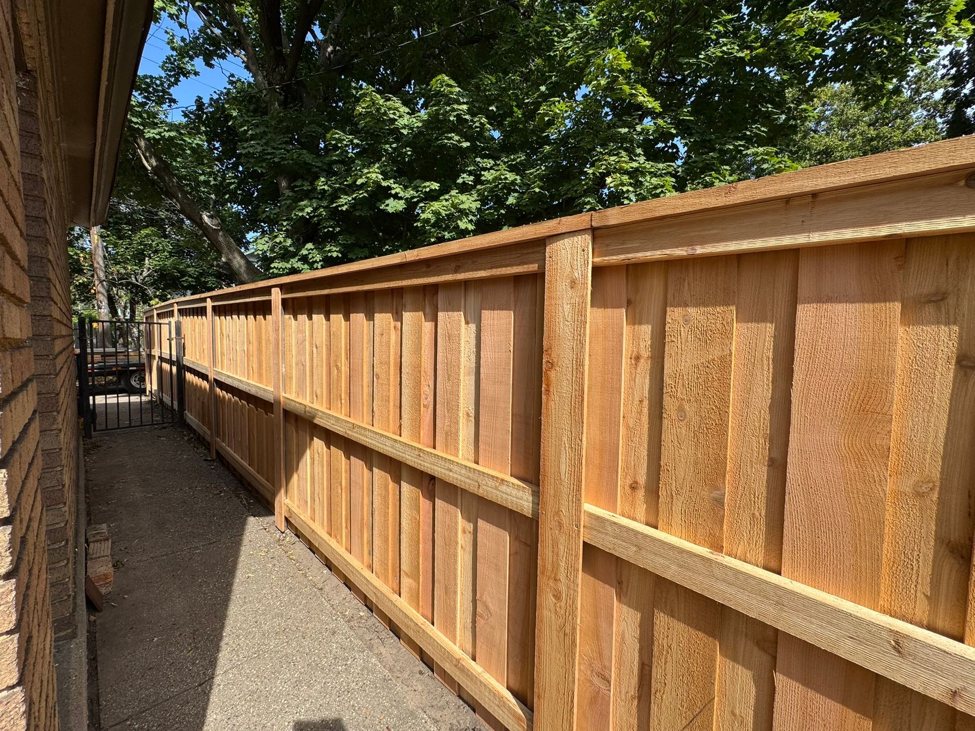 Wooden fence next to a building and gravel path, under a blue sky.