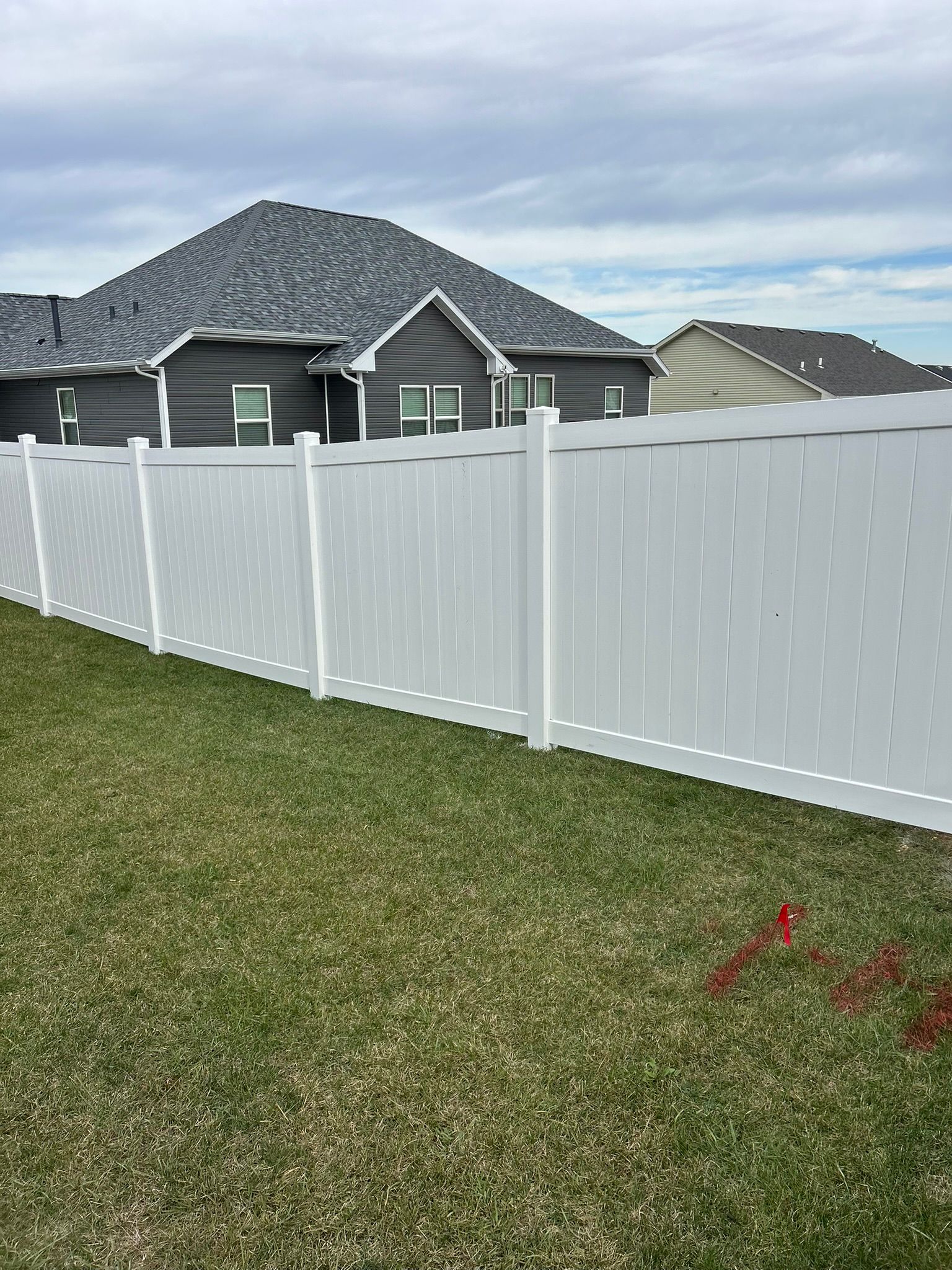 White vinyl fence in a grassy yard, with houses in the background under a cloudy sky.