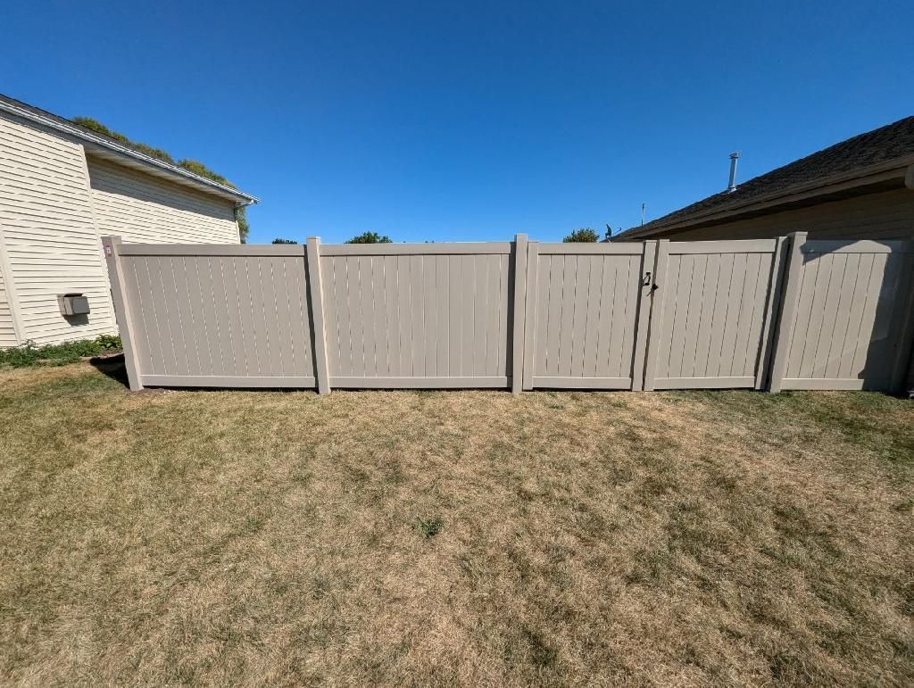 Tan vinyl privacy fence between two houses under a blue sky.