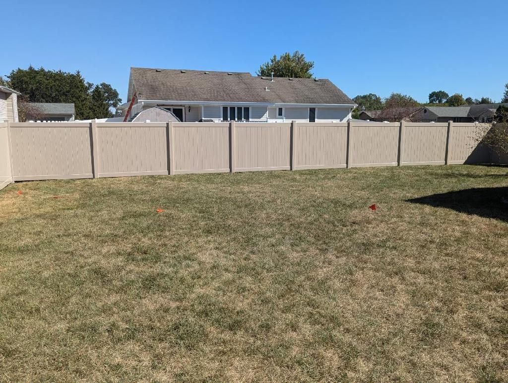 A backyard with a beige fence and a house in the background on a sunny day.