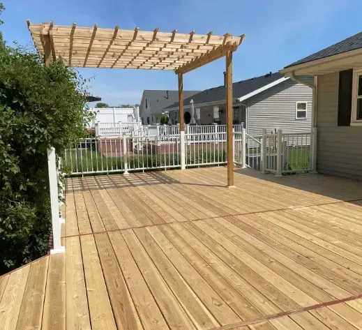 Wooden deck with pergola, white fence, and house in backyard setting.