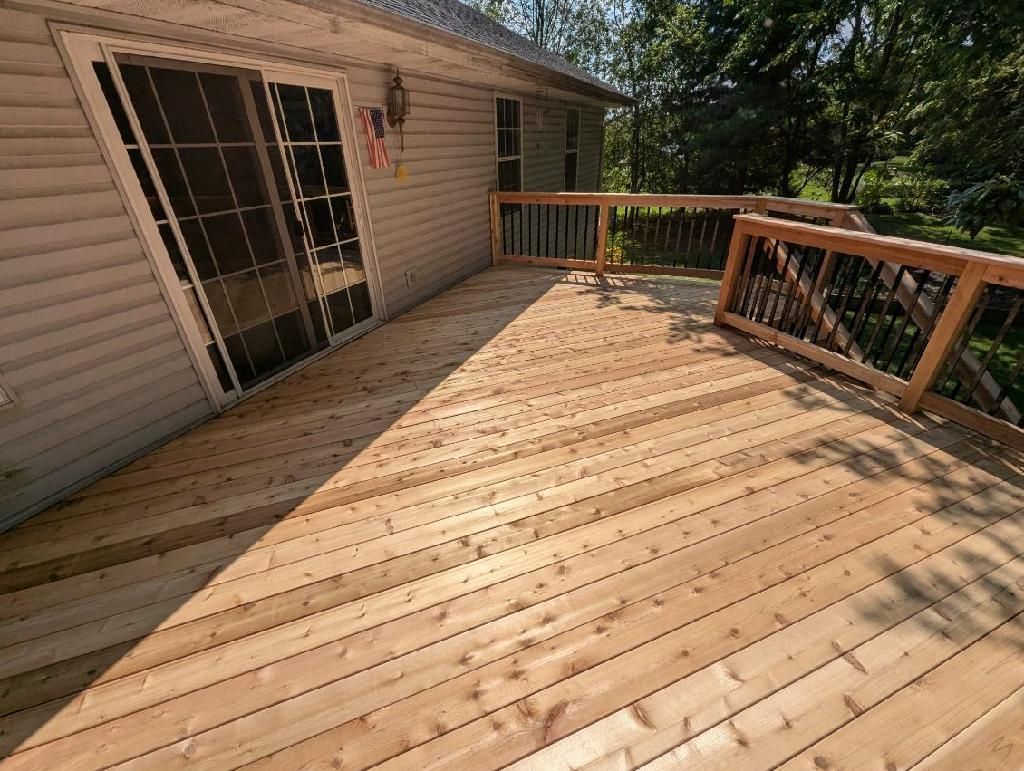 Wooden deck attached to a house with a sliding glass door, in a sunny outdoor setting.