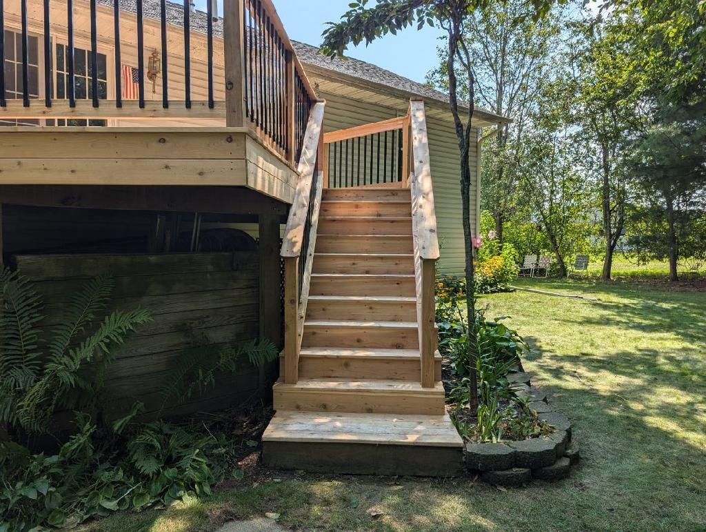 Wooden deck with stairs leading to a backyard. The deck and stairs are made of light-colored wood.
