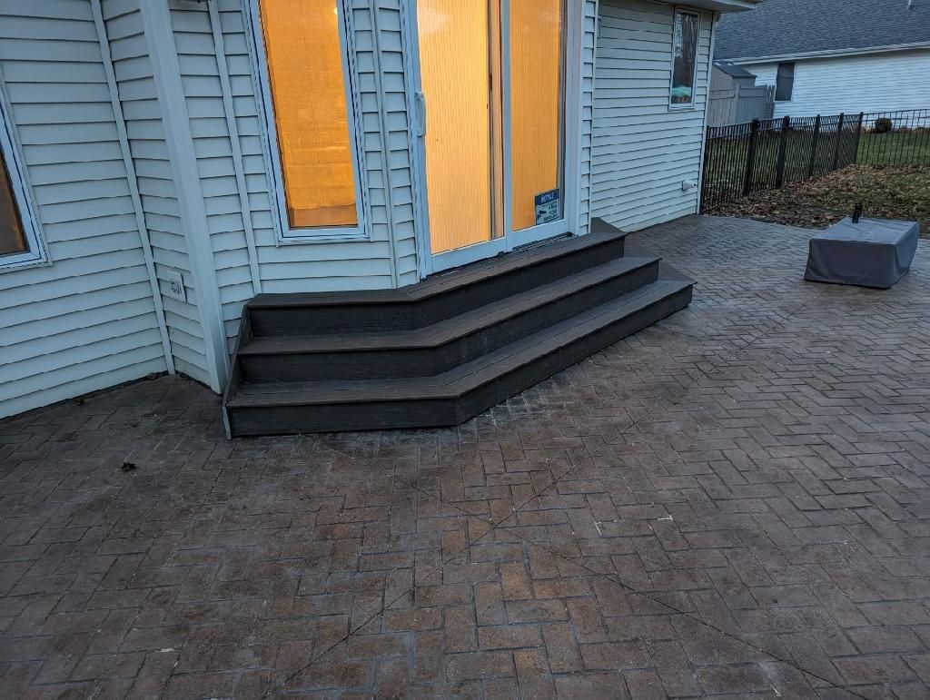 Dark steps leading up to sliding glass doors, surrounded by patterned concrete patio.