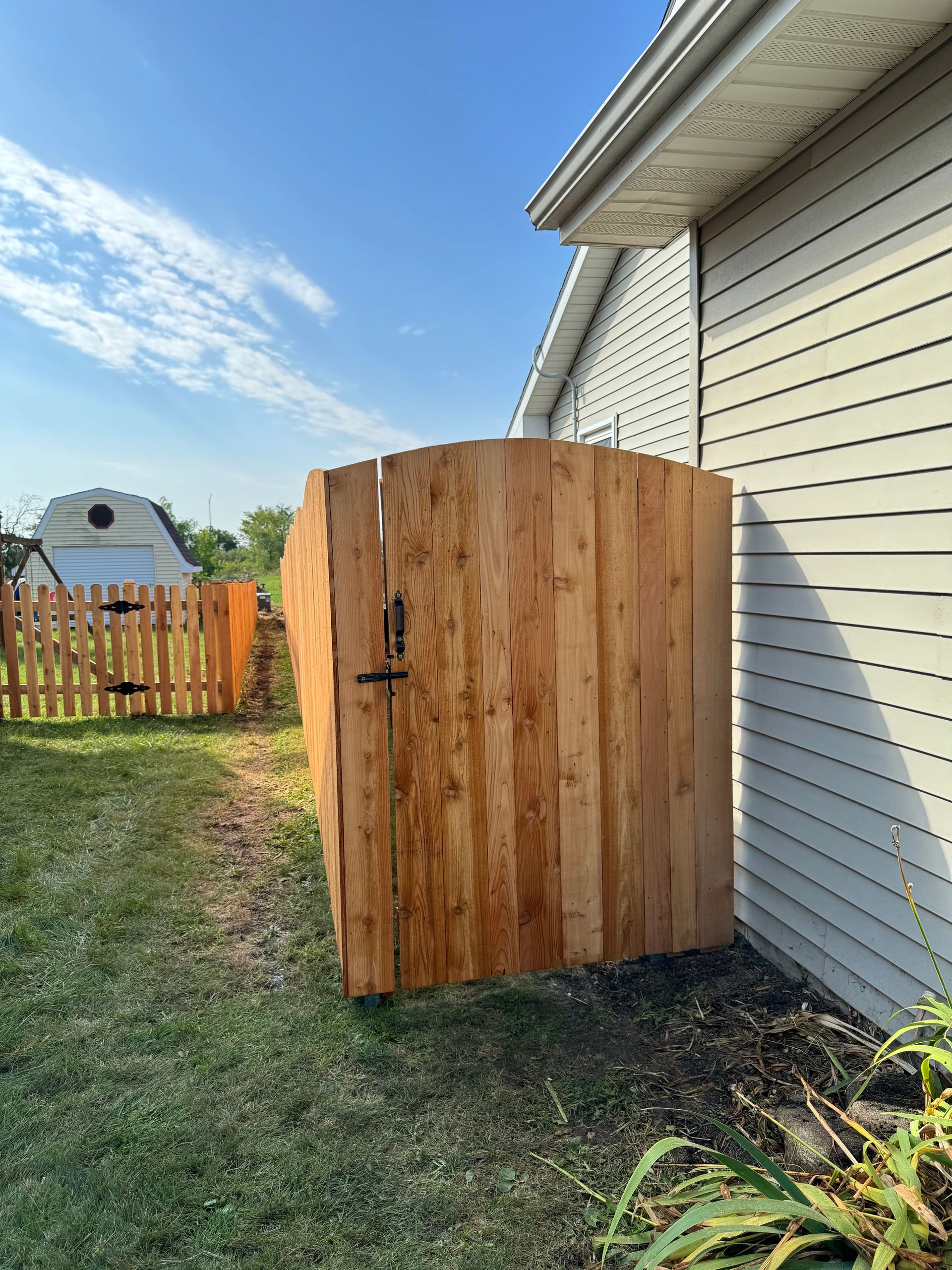 Wooden enclosure next to a house with a green lawn and a fence under a blue sky.