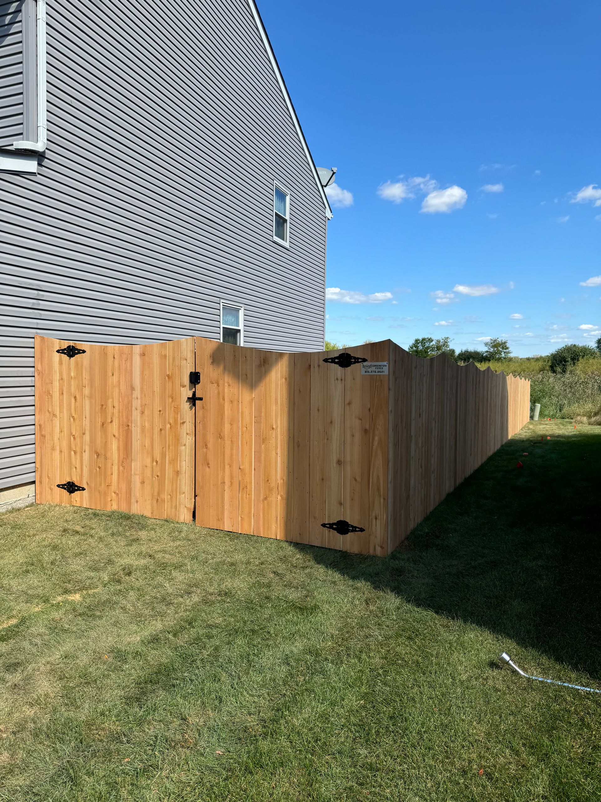 Wooden fence along a gray house on a sunny day.