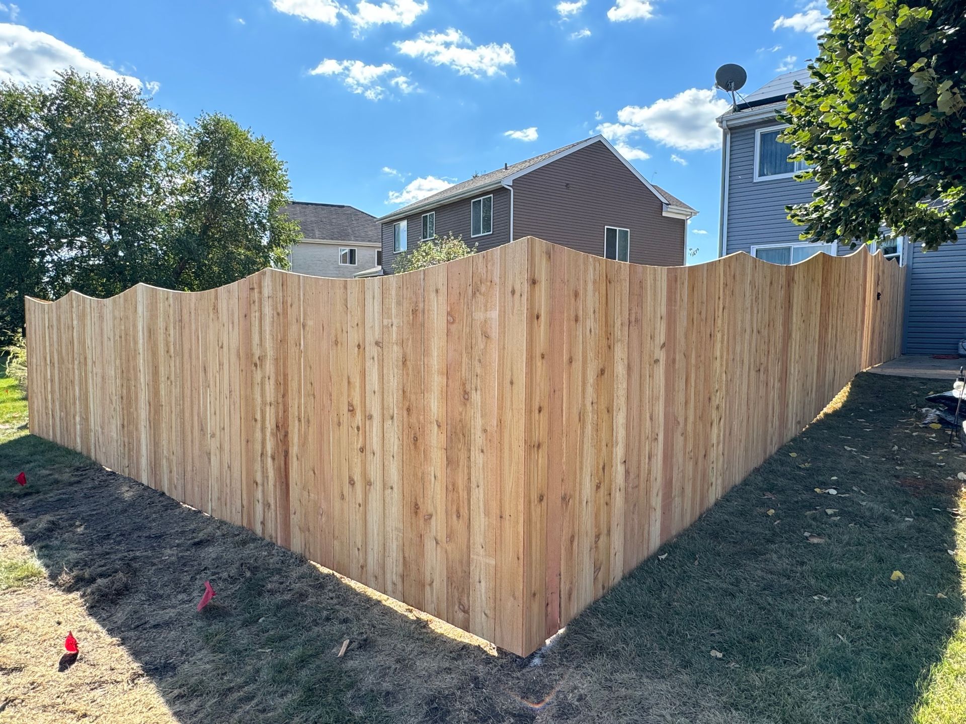 Wooden fence enclosing a backyard with houses in the background on a sunny day.