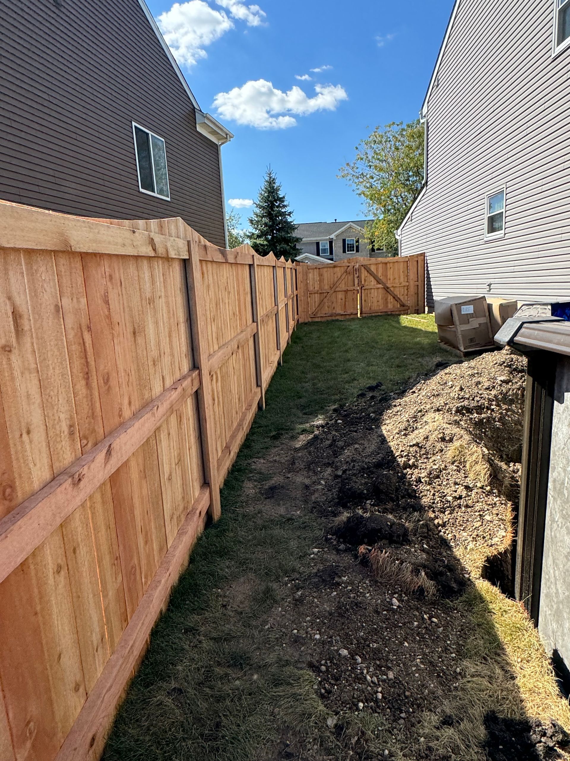Wooden fence in a backyard, with a lawn and a partially exposed shed, under a blue sky.