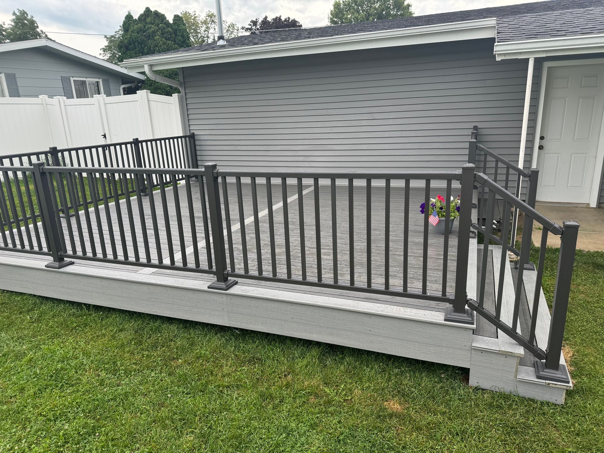 Gray deck with dark gray railings, flower pots, and siding. Green lawn.