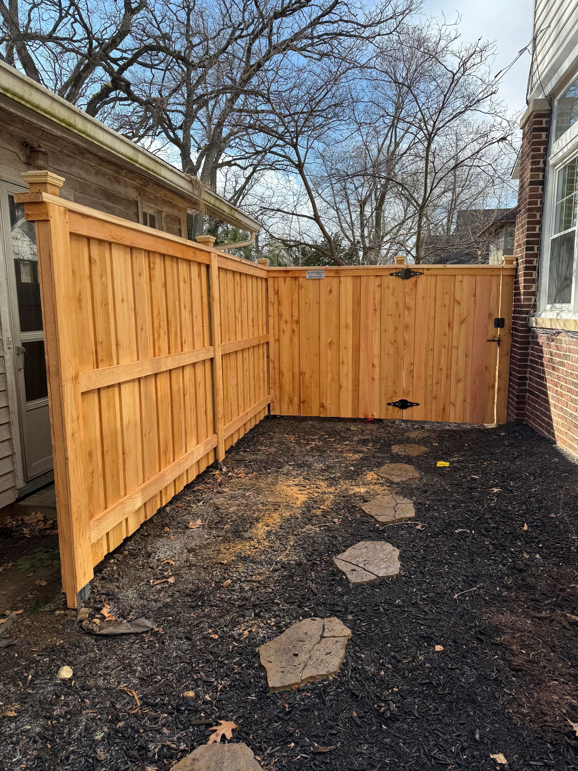 Wooden fence surrounds a small yard space with stepping stones and black mulch.