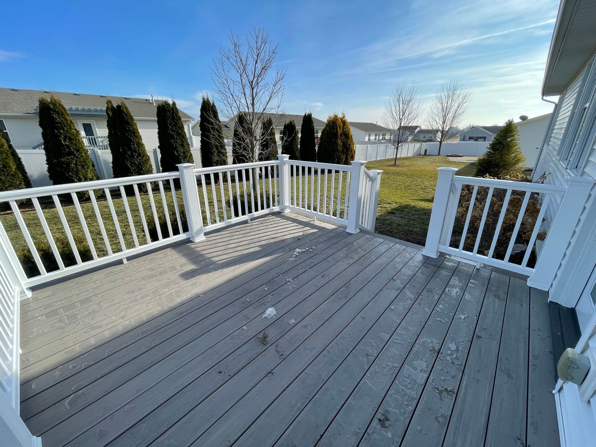 Gray wooden deck with white railing, sunny day, backyard view.