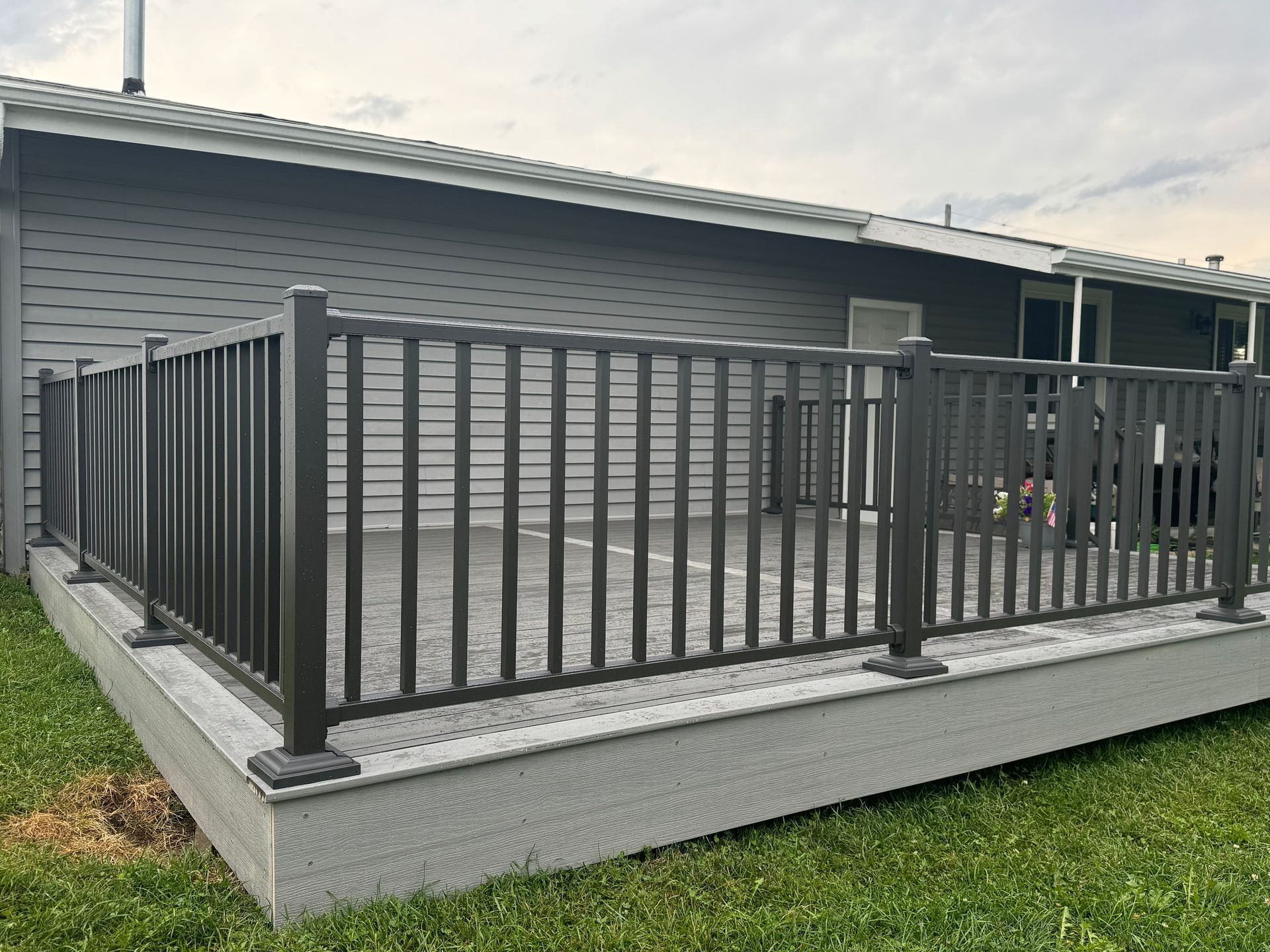 Dark gray deck with matching railing, set against a house with gray siding and green lawn.