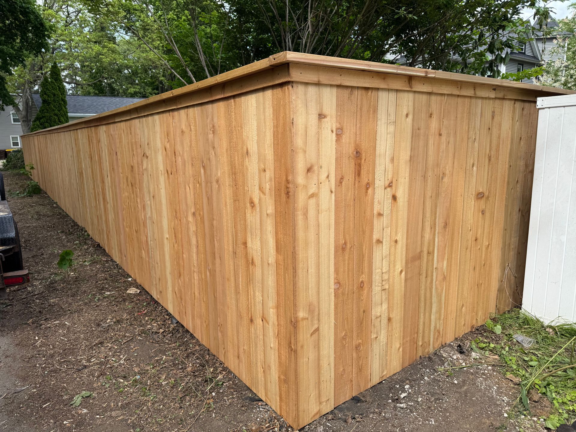 Wooden fence, newly built, surrounds a property with trees in the background.