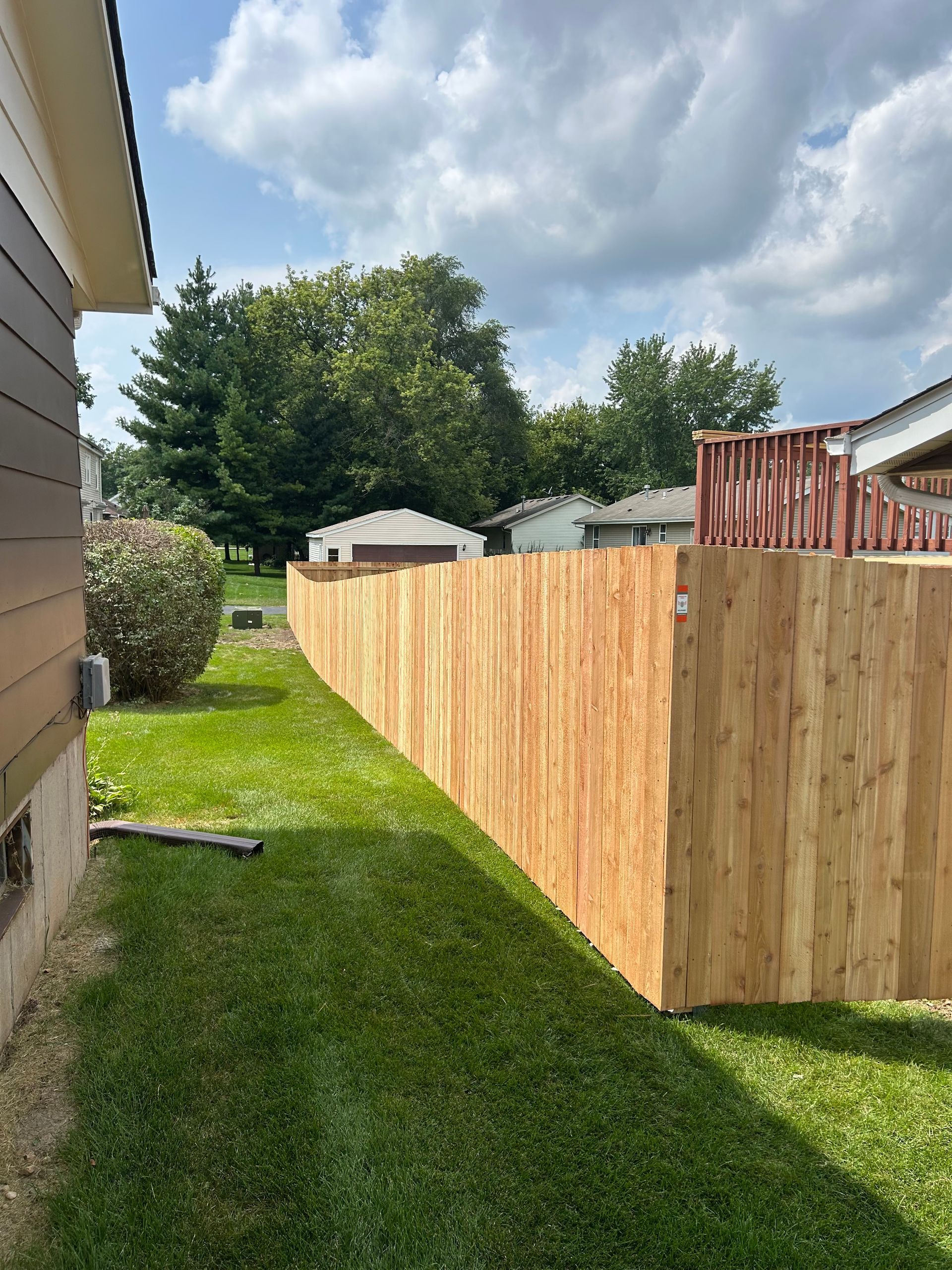 Wooden fence in backyard on a sunny day with green grass and a house.