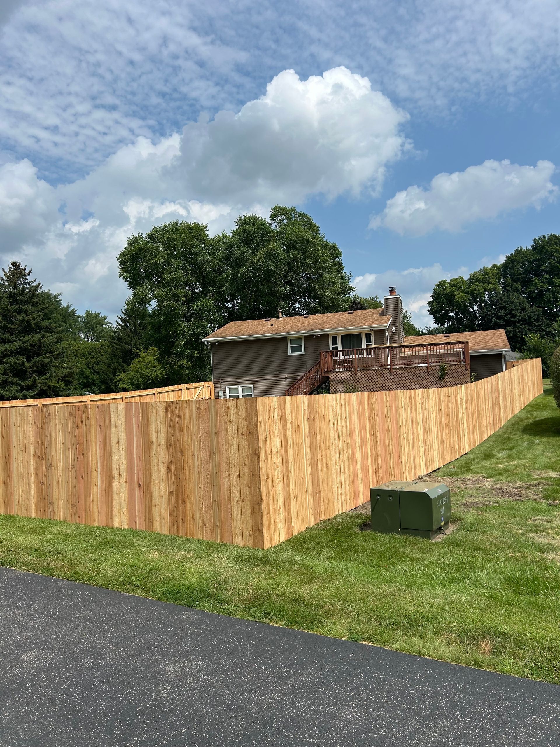 Wooden fence surrounding a house with a green lawn under a partly cloudy sky.