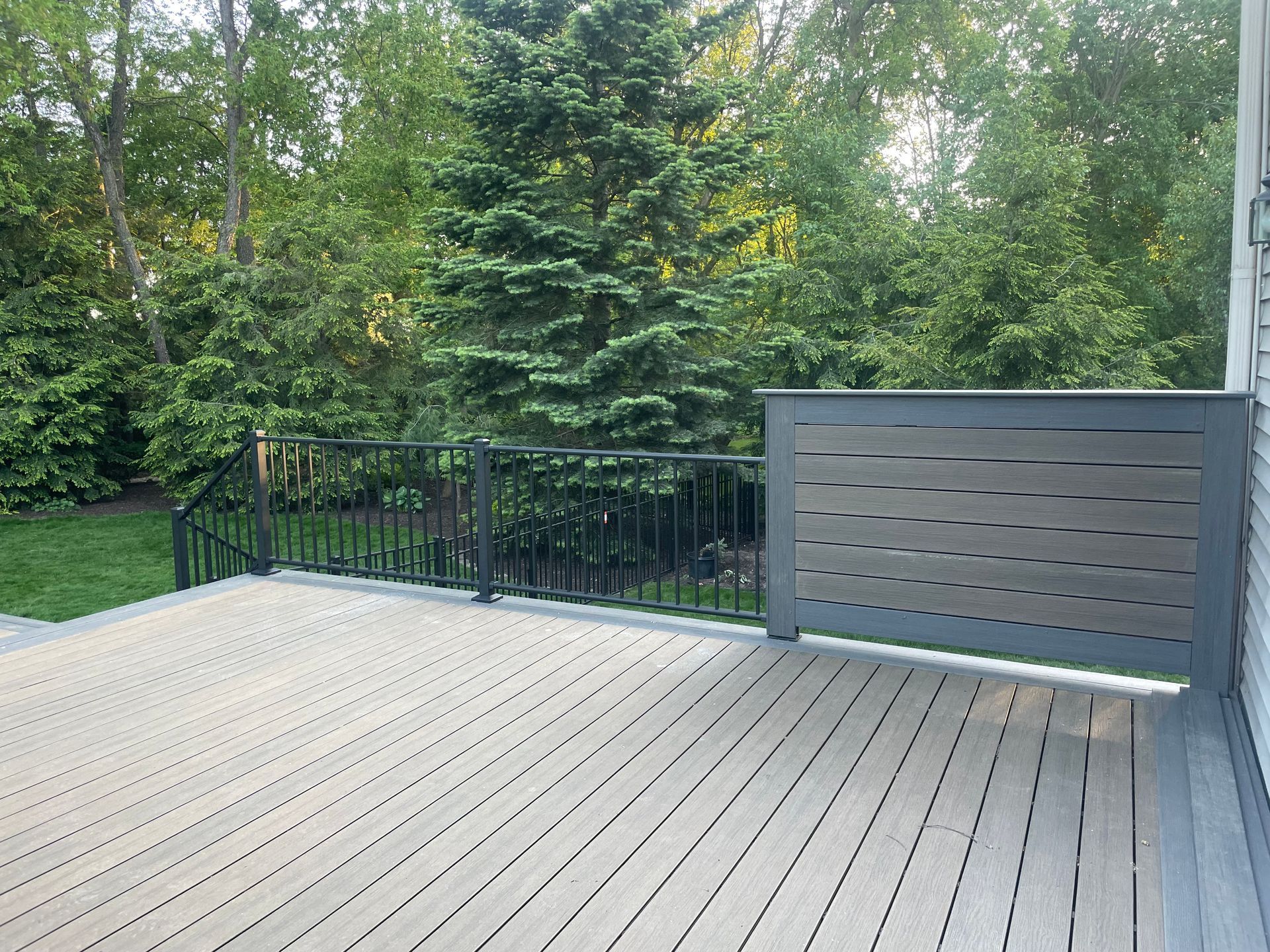 Wooden deck with gray and black railing, surrounded by trees.