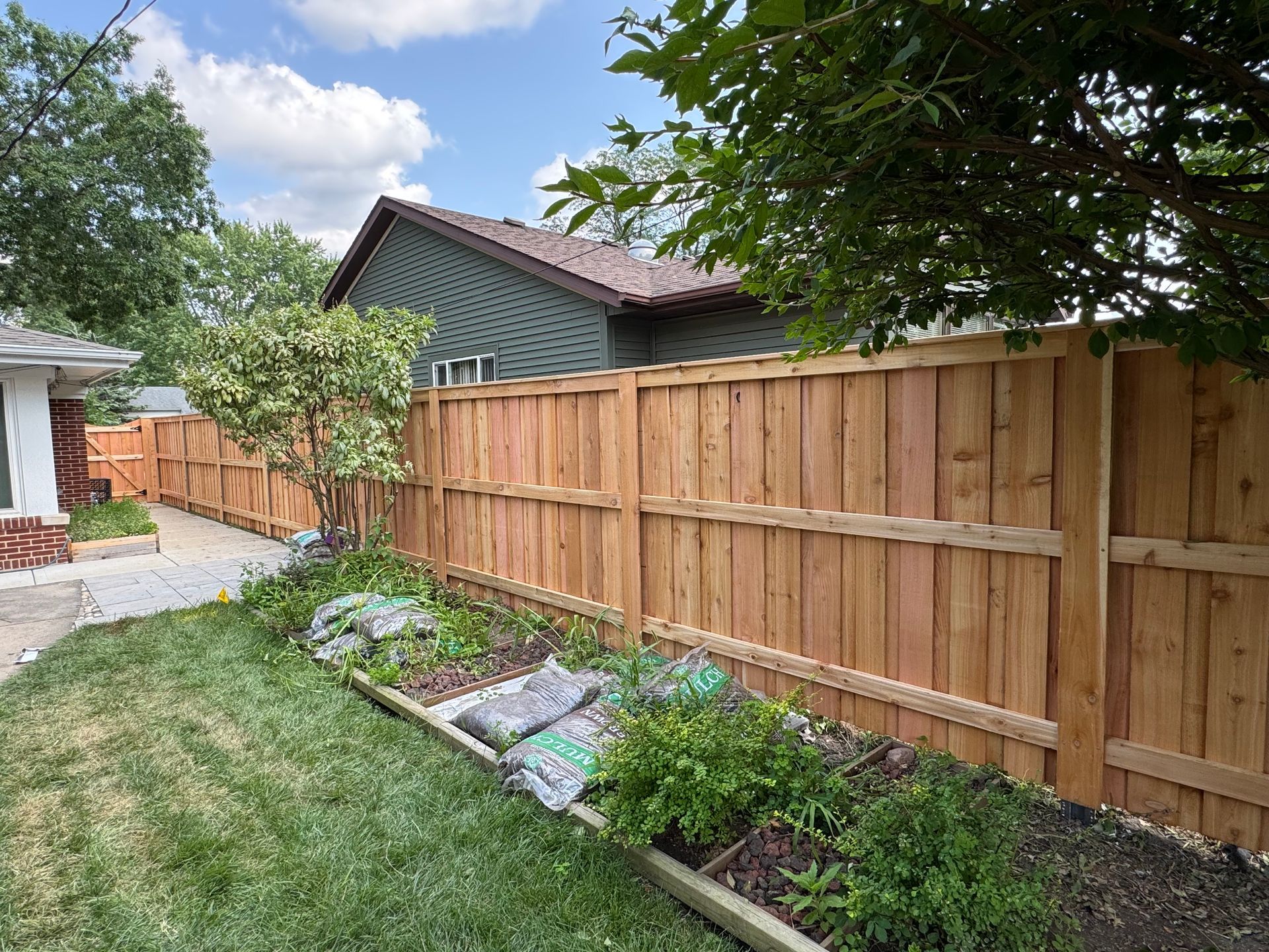 Wooden privacy fence bordering a backyard with grass, flowers, and a house.